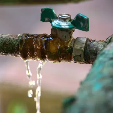 Cano metálico antigo com registro vazando água, sinal de vazamento a localizar