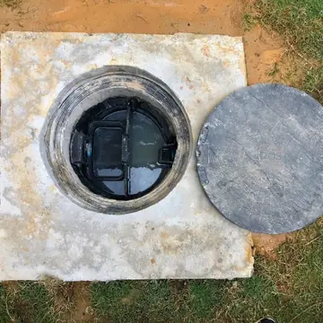 Caixa de gordura aberta no chão com tampa de concreto ao lado durante limpeza