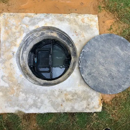 Caixa de gordura aberta no chão com tampa de concreto ao lado durante limpeza