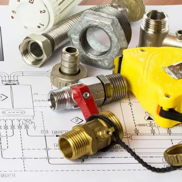 Conexões de latão, trena e planta técnica sobre a mesa durante elaboração de projeto hidráulico