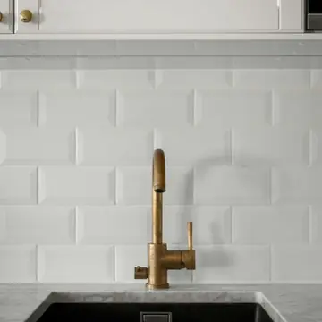 Torneira dourada de bancada instalada em cozinha com azulejo branco após instalação profissional