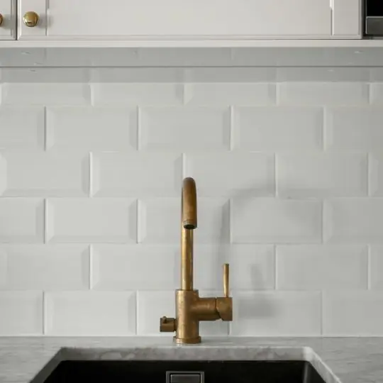 Torneira dourada de bancada instalada em cozinha com azulejo branco após instalação profissional