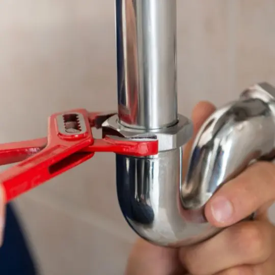 Mãos com chave grifo vermelha apertando conexão cromada durante troca de reparo de registro